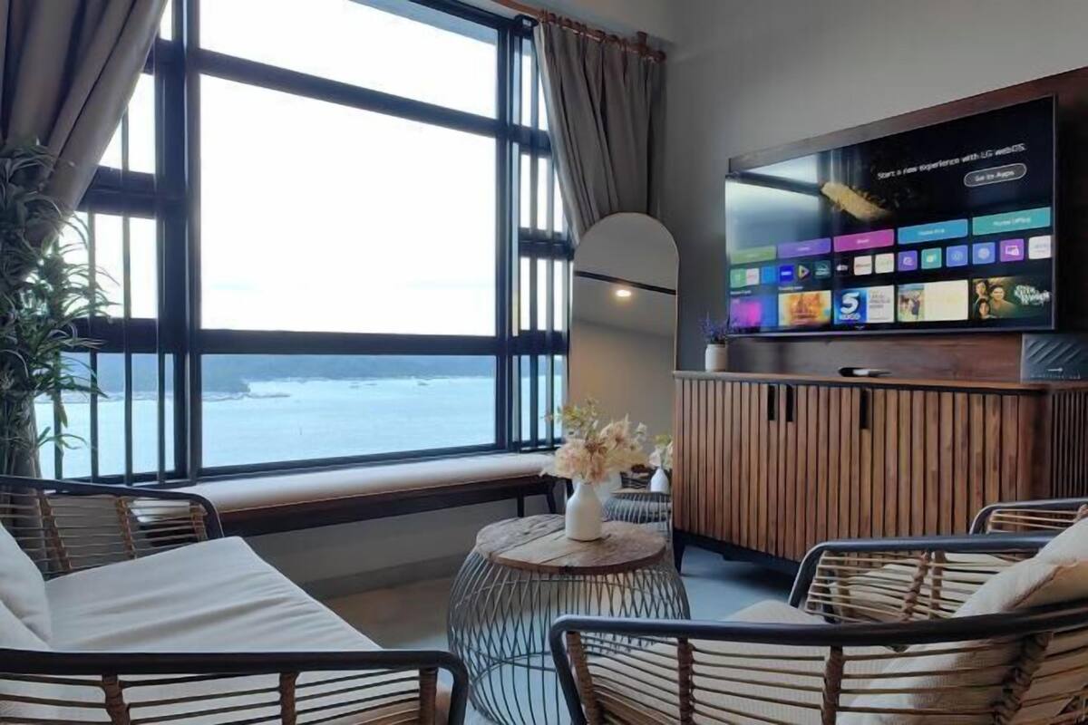 Een kamer met een groot raam met uitzicht op zee, een flatscreen televisie aan de muur en een ronde houten tafel met een bloevas.