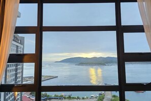 A view through a window with a grid pattern, overlooking a body of water with a distant landmass and buildings. - JESSELTON QUAYFULL SEA VIEWHIGH FLOORCOMFORT2BR4 PAX (Kota Kinabalu)