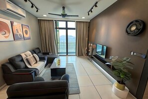 A modern living room with a sofa set, a coffee table, a TV, and a potted plant. - Green Haven Three-Bedroom (Plentong)