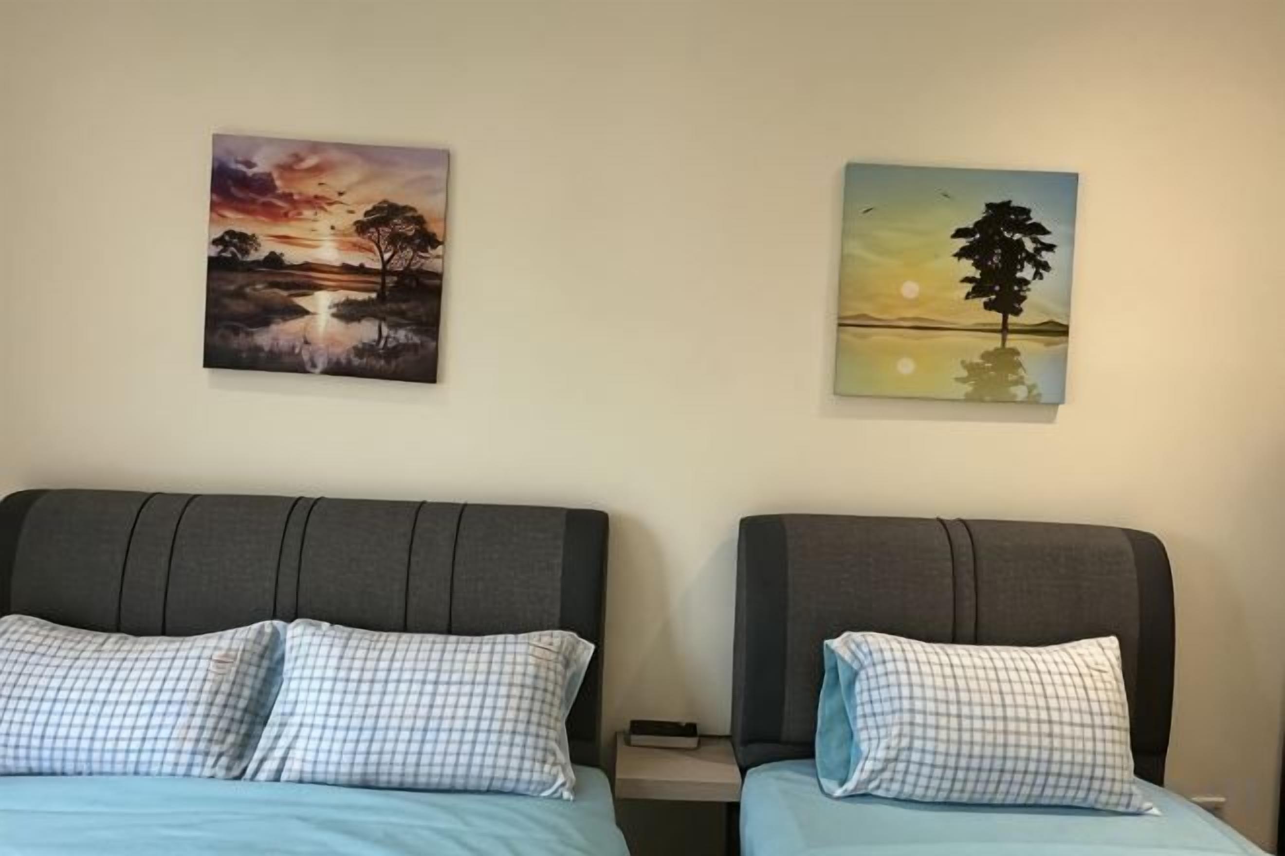 Une chambre d’hôtel avec deux lits, chacun agrémenté d’un oreiller à carreaux et d’une tête de lit. Deux tableaux représentant des paysages sont accrochés au mur.