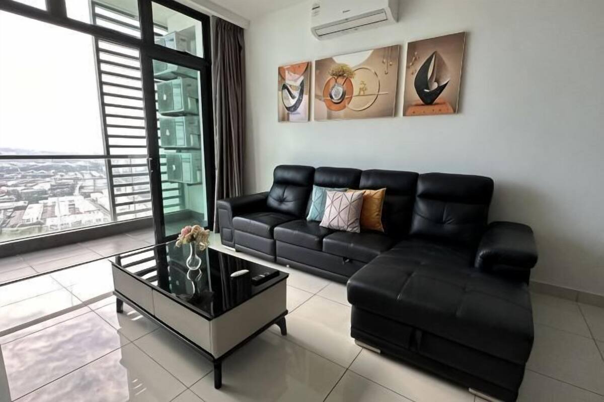 A modern living room with a black leather sofa, a glass coffee table, and artwork on the wall.