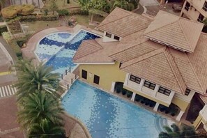 A building with a swimming pool, a palm tree, and a tiled roof. - Near Manila Airport, "Hotel Style" Studio Condo With Kitchen + Pool, 5G (Paranaque)