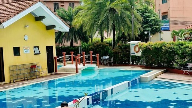 Une piscine avec une terrasse en bois, un bâtiment jaune et des palmiers.