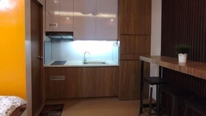 Une cuisine de taille réduite, avec des meubles de rangement en bois, un évier et un tabouret de bar.