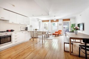 A modern kitchen with white cabinetry, a dining area with a wooden table and chairs, and a view of the outdoors. - NOA - Tatar Beyi 18 (Istanbul)