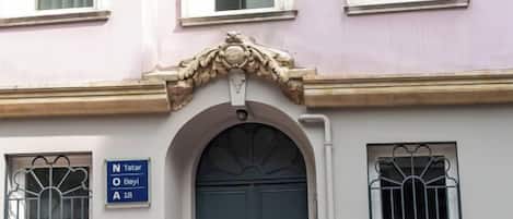 A building facade with a large arched entrance, a sign indicating the name 'N Tatar' and 'Bey' with a number '18' below, and a window with a metal grill.