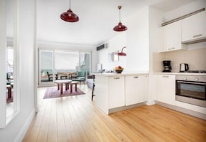 A modern kitchen with white cabinets, a wooden floor, and a dining area with a table and chairs. - NOA - Tatar Beyi 18 (Istanbul)