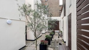 A narrow alleyway with potted plants, a wooden bench, and a white wall. - Kula London - Victoria (London)