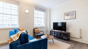 A living room with a sofa, a coffee table, a TV, and a radiator. - Kula London - Victoria (London)