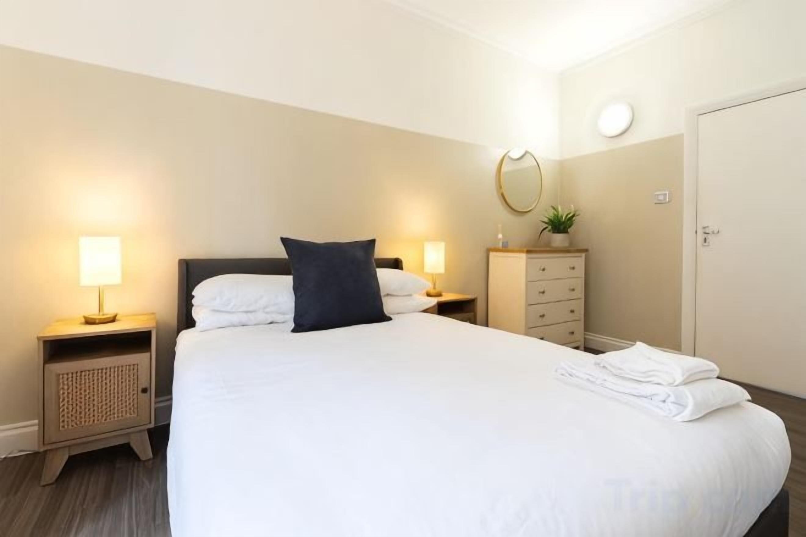 A hotel room with a large bed, bedside lamps, a dresser, a mirror, and a door.