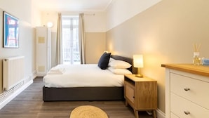 A hotel room with a bed, bedside table, lamp, and a view of the city. - Kula London - Victoria (London)