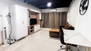 A modern living room with a flat-screen TV, a sofa, a dining table, and a vacuum cleaner. - uouRangnamHouse (Bangkok)