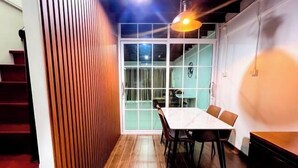 A room with a wooden floor, a white table with chairs, a staircase, and a door leading to another room. - uouRangnamHouse (Bangkok)