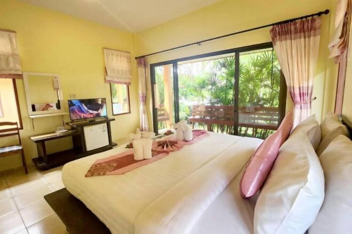 Ein Hotelzimmer mit Bett, Fernseher, Schreibtisch und Fenster mit Blick auf Grünfläche.
