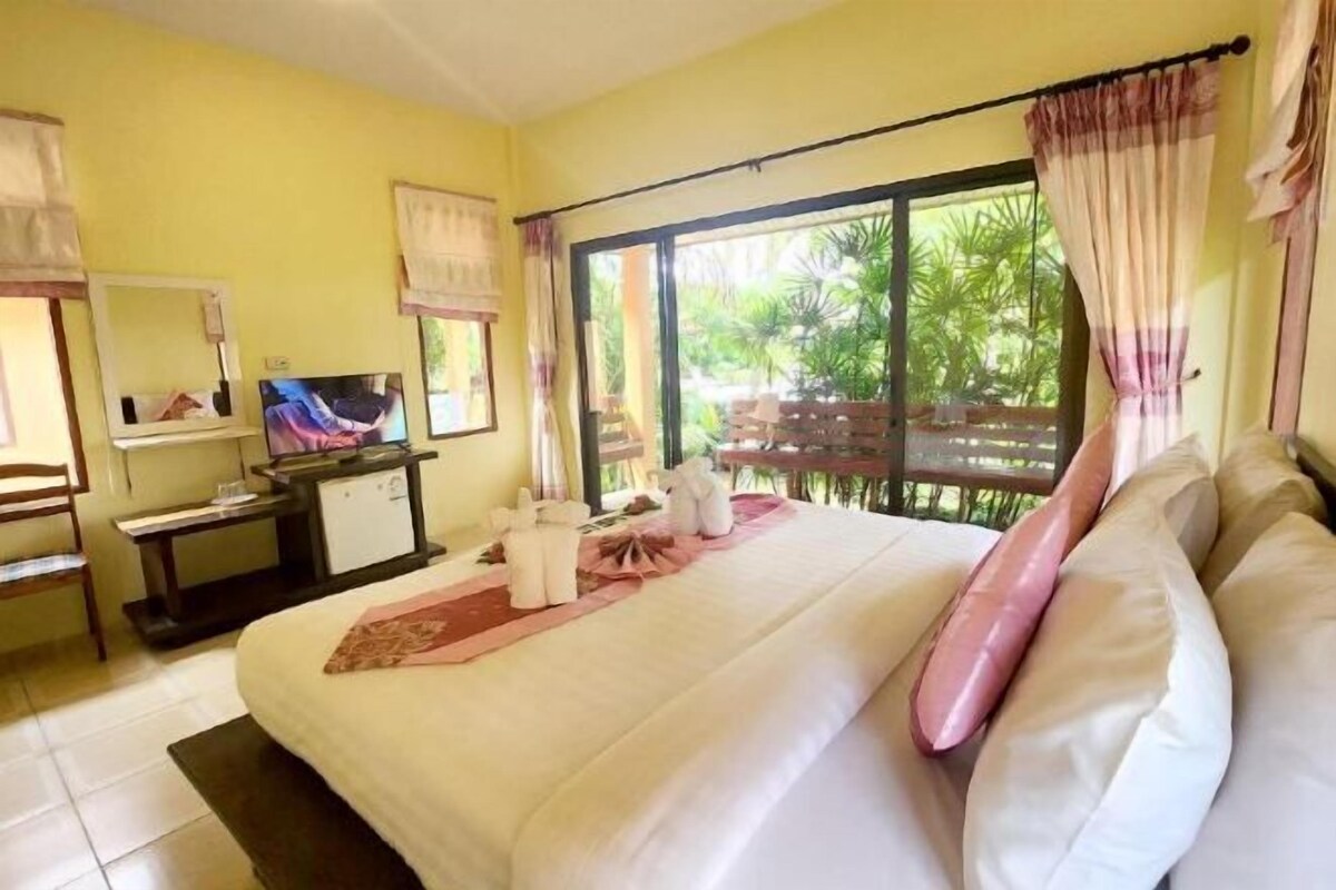 Ein Hotelzimmer mit Bett, Fernseher, Schreibtisch und Fenster mit Blick ins Grüne.
