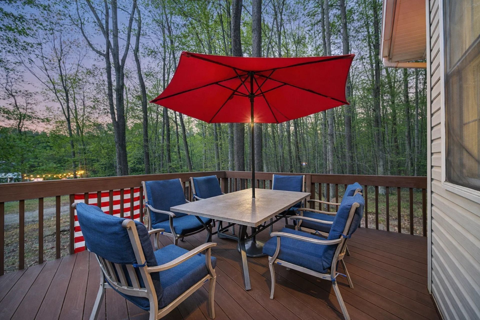 A deck with a table and chairs, a red umbrella, and a view of trees.