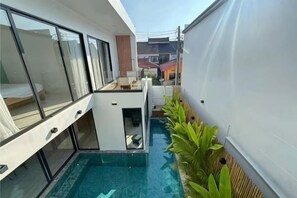 En modern byggnad med en balkong i glas, en liten pool och en rad med växter.