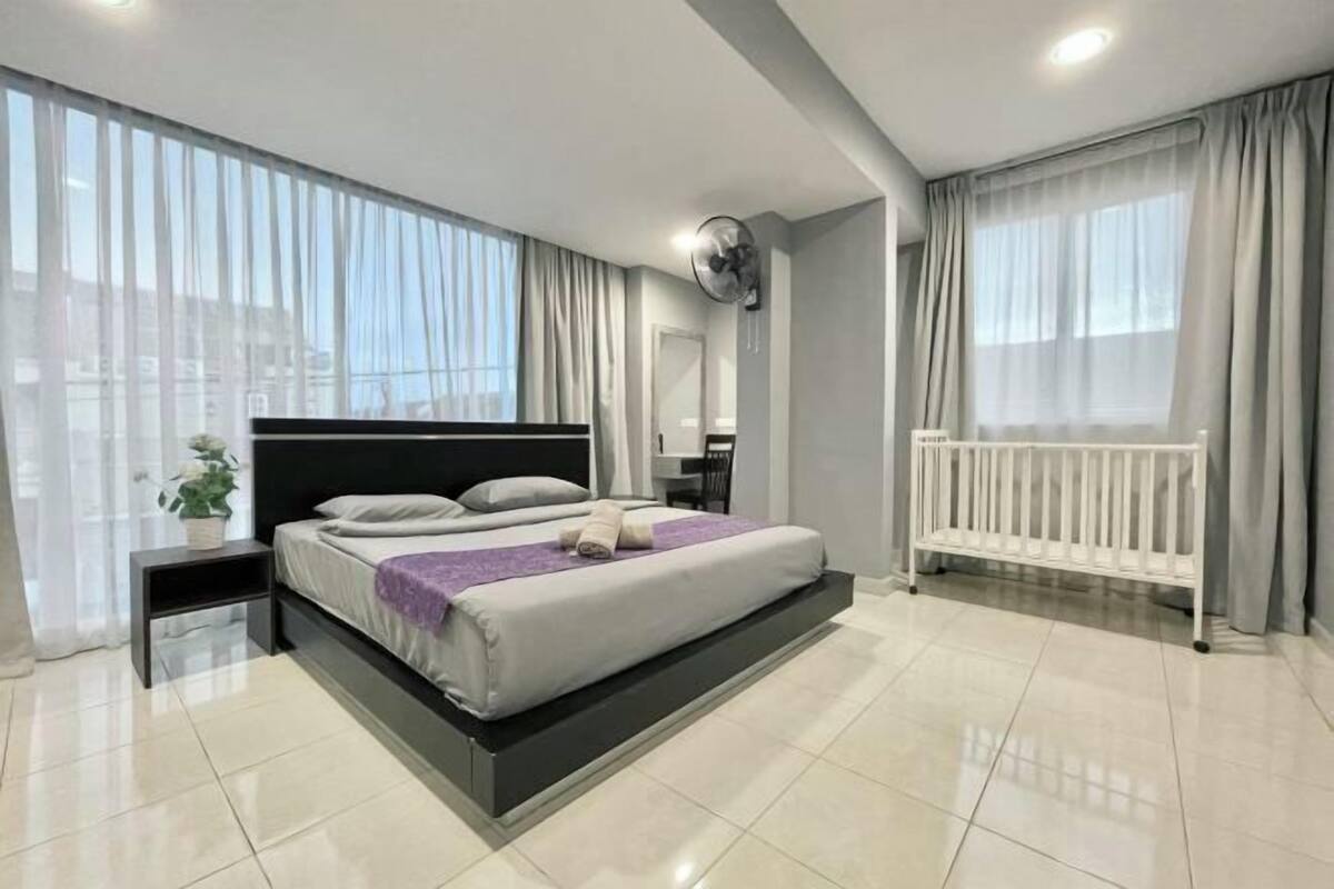 A modern bedroom with a large bed, a bedside table, a wall-mounted fan, and a window with curtains.