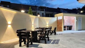 Eine Terrasse im Freien mit Tischen und Stühlen, eine Ziegelwand und ein Gebäude im Hintergrund.
