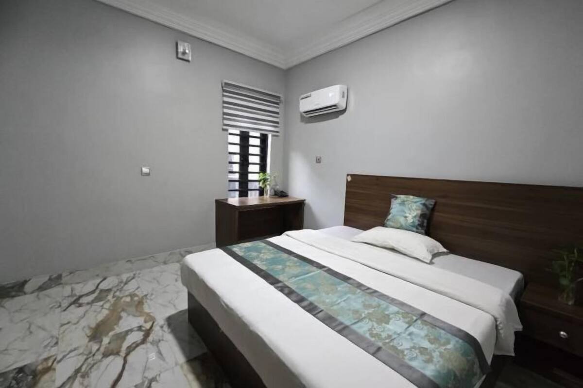 A bedroom with a bed, nightstand, and window with blinds.