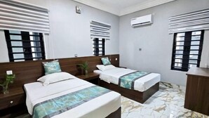 Hotellihuone, jossa on kaksi sänkyä, puinen pääty, marmorilattia ja pieni kasvi yöpöydällä.