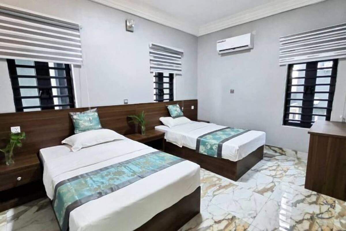 A hotel room with two beds, a wooden headboard, a marble floor, and a small plant on the nightstand.