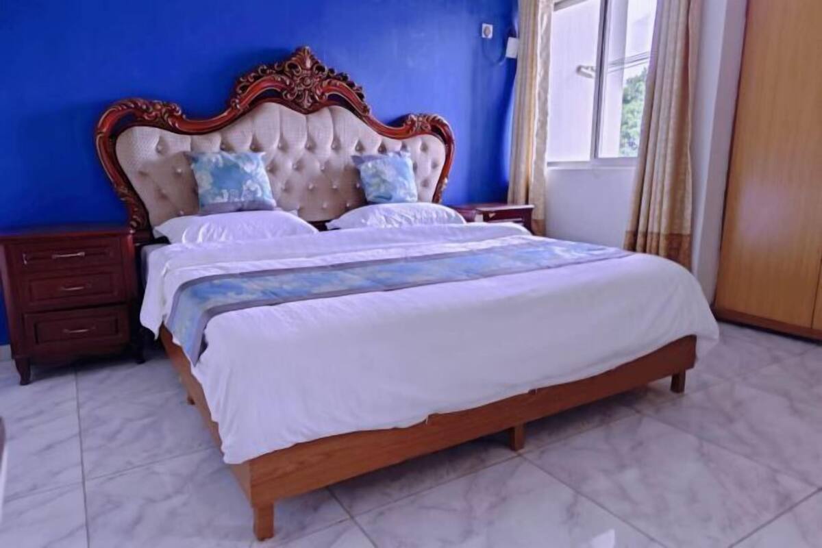 A bedroom with a large bed, wooden headboard, two nightstands, a dresser, and a window with curtains.
