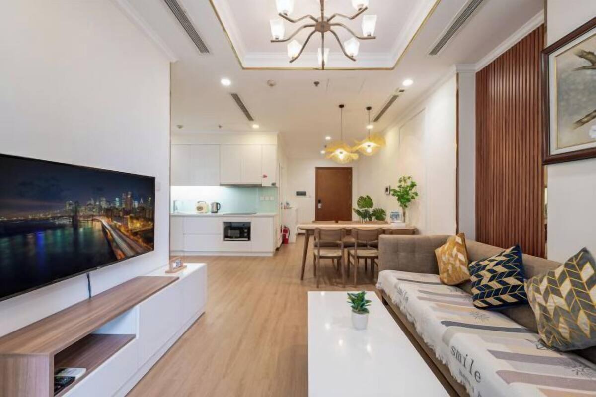 A modern living room with a flat-screen TV, a sofa, a coffee table, and a dining area with a table and chairs.