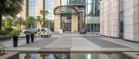 Un bâtiment moderne avec un bassin d’eau réfléchissante en premier plan, de grandes fenêtres en verre et une entrée incurvée.