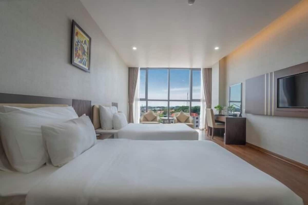 A hotel room with two beds, a TV, and a large window offering a city view.