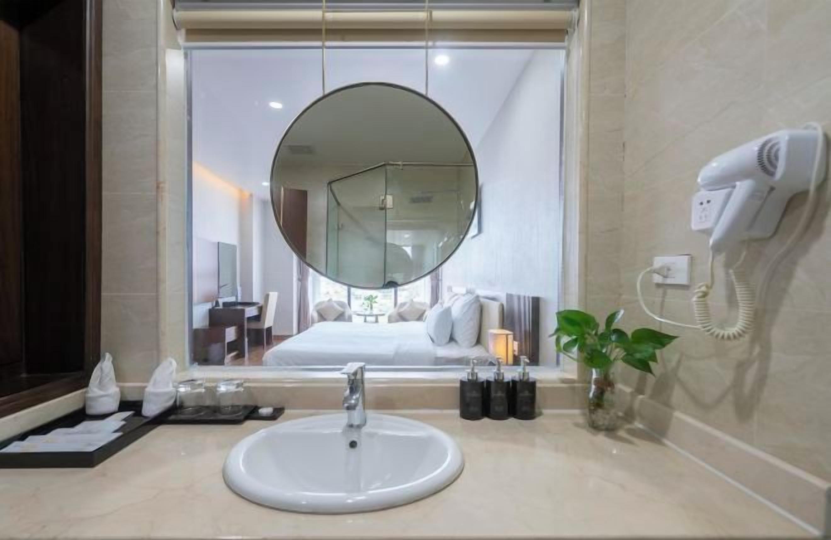 A bathroom with a round mirror, a sink, a hairdryer, and a potted plant.