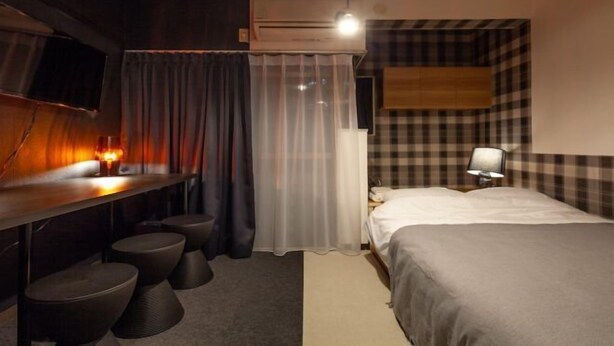 A hotel room with a bed, a desk with a chair, a TV, and a window with curtains.