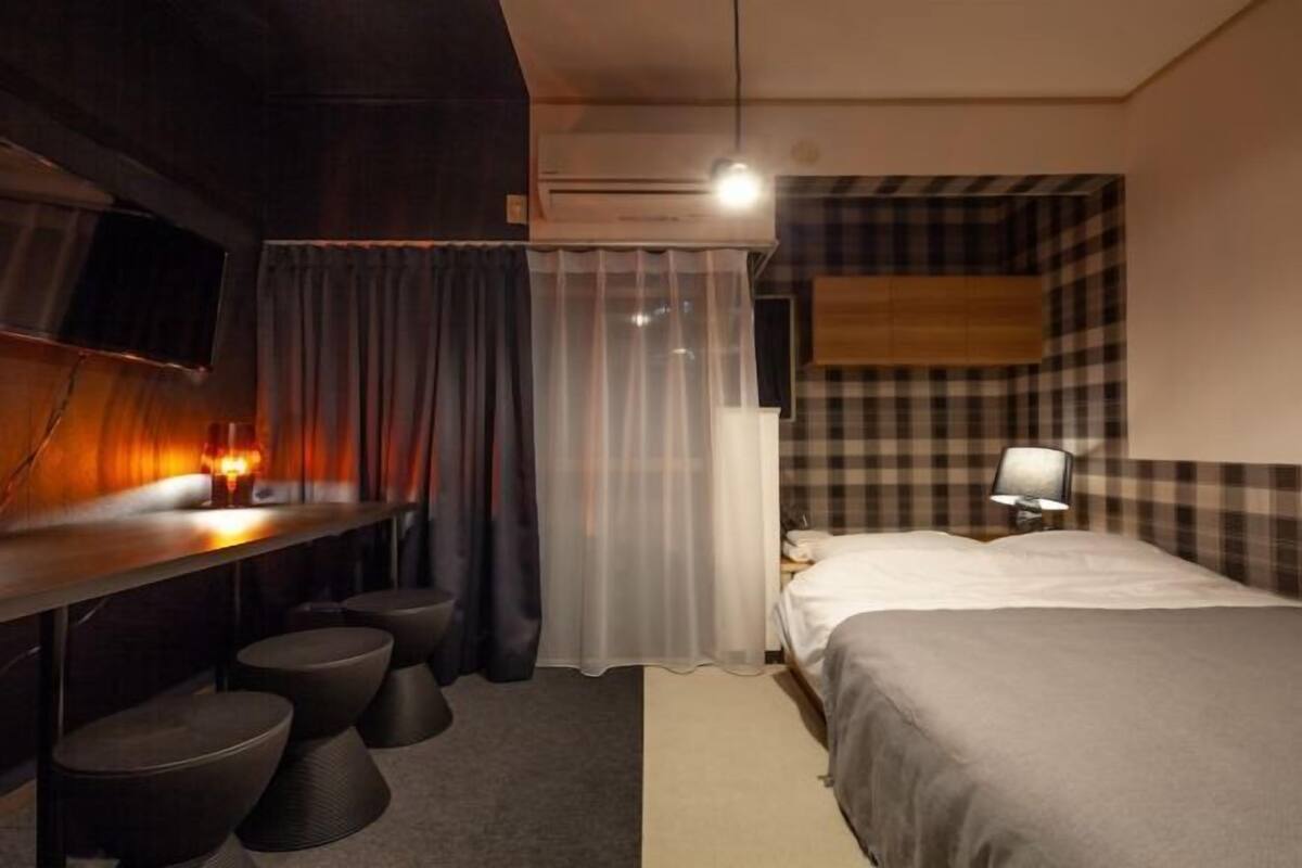 Ein Hotelzimmer mit einem Bett, einem Schreibtisch mit Stuhl, einem Fernseher und einem Fenster mit Vorhängen.