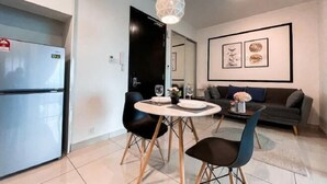 A modern kitchen with a built-in refrigerator, a dining area with a round table and chairs, a sofa, and a pendant light. - Almas Puteri Harbour Nusajaya Suite Room Exclusive Room 5 Min to Legoaland by HomeSpace (Iskandar Puteri)