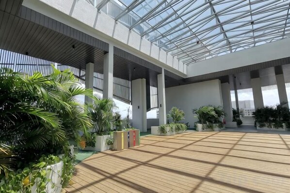 Amplio espacio interior con techo alto y cubierta de vidrio, suelo de madera y plantas en macetas.