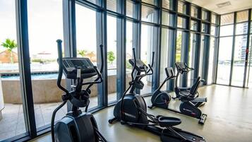 Une salle de sport équipée de vélos d’appartement et de tapis de course, dotée de grandes fenêtres et offrant une vue sur l’extérieur.