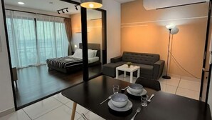 A hotel room with a bed, a sofa, a dining table with plates and cutlery, a mirror, and a lamp. - Almas Puteri Harbour Nusajaya Suite Room Exclusive Room 5 Min to Legoaland by HomeSpace (Iskandar Puteri)