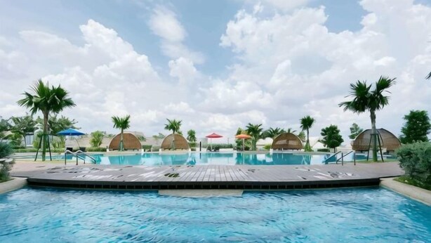 A swimming pool with lounge chairs and umbrellas, surrounded by palm trees and covered structures. - Almas Puteri Harbour Nusajaya Suite Room Exclusive Room 5 Min to Legoaland by HomeSpace (Iskandar Puteri)