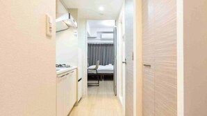 A narrow hallway leading to a bedroom with a bed, a chair, and a small kitchenette area. - EST Swan's City Shinsaibashi East Shimanouchi (Osaka)