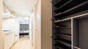 A narrow hallway with a kitchen area on the left, a bed with a chair in the middle, and a built-in shoe rack on the right. - EST Swan's City Shinsaibashi East Shimanouchi (Osaka)