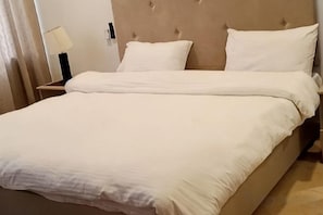 Una cama con cabecera, una mesita de noche con lámpara y un espejo.