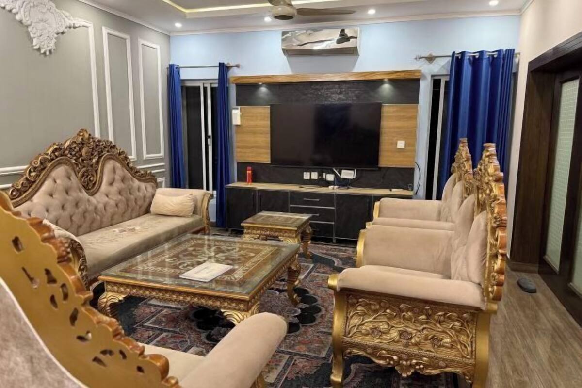 A luxurious living room with a large flat-screen TV, ornate furniture, and a patterned carpet.