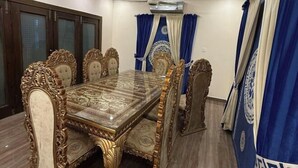 A dining area with a large ornate table and matching chairs, a ceiling fan, and blue curtains. - AoLai Hotel (Islamabad)