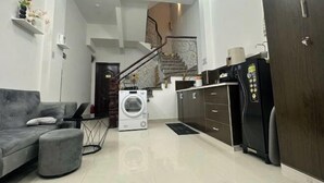 A modern living room with a grey sofa, a washing machine, a refrigerator, and a staircase leading to an upper floor. - Aesthetic homes Bui Vien Street (Ho Chi Minh City)