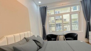 A hotel room with a bed, a small table, two chairs, a window with curtains, and a balcony view. - Aesthetic homes Bui Vien Street (Ho Chi Minh City)