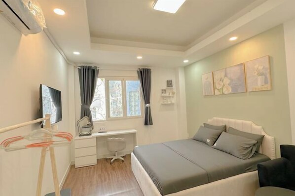 A bedroom with a bed, a desk, a chair, a TV, and a window with curtains.
