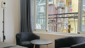 A room with a bed, two armchairs, a small table, a window with a view of buildings, and a security camera. - Aesthetic homes Bui Vien Street (Ho Chi Minh City)