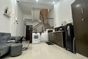 Un espace de vie compact comprenant un canapé, un lave-linge, un réfrigérateur et un escalier menant à un niveau supérieur.