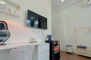 Une chambre d’hôtel comprenant un lit, un bureau avec une chaise, un téléviseur fixé au mur, une petite poubelle et une étagère avec des objets décoratifs.