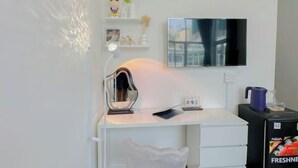 A modern room with a white desk, a mounted TV, a small shelf with decorative items, a clock, and a refrigerator with a water dispenser. - Aesthetic homes Bui Vien Street (Ho Chi Minh City)